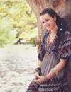 Cute smiling hippie indie style woman with dreadlocks, dressed in boho style ornamental dress posing outdoor