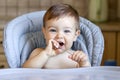 Cute smiling hungry little boy holding spoon and playing with it waiting for food, looking at camera