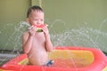 Asian boy child eating watermelon in summertime, Little kid having fun playing with splash water at home