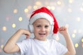 Cute smiling little boy in a Christmas red cap and headphones, listening to music, he`s happy. Light background, bokeh