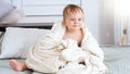 Cute smiling little boy covered in white towel after bath sitting on bed Royalty Free Stock Photo