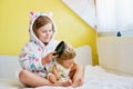 Cute smiling little girl child playing with her doll at home. Preschool child in bathrobe after taking bath brushing Royalty Free Stock Photo