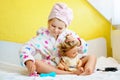 Cute smiling little girl child playing with her doll at home. Preschool child in bathrobe after taking bath brushing Royalty Free Stock Photo