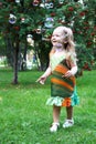 Cute smiling little girl in colorful sundress is playing with soap bubbles in summer park Royalty Free Stock Photo