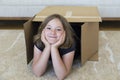 Cute smiling little girl lying down in plain brown house moving cardboard box Royalty Free Stock Photo