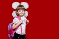 Cute smiling little girl in school uniform and white bows with backpack on red background. Back to school Royalty Free Stock Photo