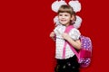 Cute smiling little girl in school uniform and white bows with backpack on red background. Back to school Royalty Free Stock Photo