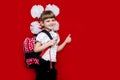 Cute smiling little girl in school uniform and white bows with backpack on red background. Back to school Royalty Free Stock Photo