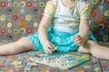 A cute smiling little girl sits on the sofa and collects a puzzle.