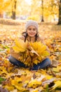 Cute smiling little girl sitting on the fallen leaves in autumn park and holding the bouquet of yellow maple leav Royalty Free Stock Photo