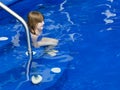 Little girl sitting in shallow water on the steps of a deep blue pool Royalty Free Stock Photo