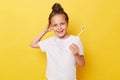Cute smiling little girl with wet hair wearing casual white T-shirt standing isolated over yellow background taking care of her Royalty Free Stock Photo