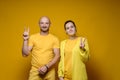 Cute, smiling man and woman in yellow clothes making a victory sign while standing against an isolated, bright Royalty Free Stock Photo