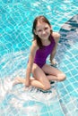 Cute smiling preteen girl sitting at swimming pool edge. Travel, vacation, childhood