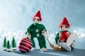 Cute Smiling Santas Helper Elves Holding Christmas Bauble and a Christmas Gift. North Pole Christmas Scene. Elves at work.