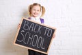 Cute smiling schoolgirl in uniform standing with blackboard and smiling. Back to school. Royalty Free Stock Photo