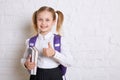 Cute smiling schoolgirl in uniform standing with books and showing ok on light background. Royalty Free Stock Photo