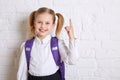 Cute smiling schoolgirl in uniform standing on light background and showing thumb up. Royalty Free Stock Photo