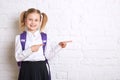 Cute smiling schoolgirl in uniform standing on light background and showing thumbs to the side. Royalty Free Stock Photo