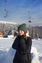 Cute smiling teenage girl in good mood stands against background of snow-covered fir trees and ski lift at a ski resort Royalty Free Stock Photo