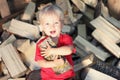 Cute smiling toddler blond boy with aspen log on the pile of firewood background. Country lifestyle. Preparation for winter season