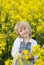 Cute smiling Ukrainian boy 6 years old in a traditional embroidered blouse among a yellow blooming rapeseed field