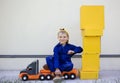 smiling 6 year old boy in blue uniform is sitting on big toy truck next to a lot of yellow cardboard boxes Royalty Free Stock Photo