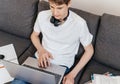 Cute smiling young teenager with laptop on the couch at home. Boy makes homework with a computer. Royalty Free Stock Photo