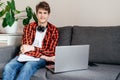 Cute smiling young teenager with laptop on the couch at home. Boy makes homework with a computer. Royalty Free Stock Photo