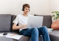 Cute smiling young teenager with laptop on the couch at home. Boy makes homework with a computer Royalty Free Stock Photo