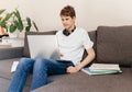 Cute smiling young teenager with laptop on the couch at home. Boy makes homework with a computer Royalty Free Stock Photo