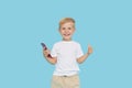 Cute smilling child boy with smartphone on blue background. Advertising of educational applications on a mobile phone