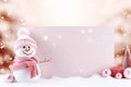 A cute snowman with a blank signboard on blurred peach fuzz background. Winter holiday banner for Christmas greetings Royalty Free Stock Photo