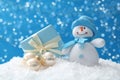 Cute snowman, Christmas balls and gift on snow against blue background, bokeh effect Royalty Free Stock Photo