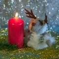 The cute soft toy in a form of a deer with the burning red candle and on the golden tinsel in the night Royalty Free Stock Photo