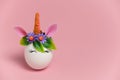 Cute spring Easter card with an unicorn egg with a rim of spring flowers and horn with copy space on a pastel pink background