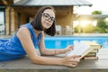 Cute student girl reading book lying near the pool. Education, summer, knowledge Royalty Free Stock Photo