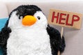 Cute stuffed toy in the shape of penguin with handmade sign with inscription HELP, front view. Call for help to