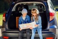 Agreeable boy and girl are looking at the road map while sitting in the auto`s trunk and discussing the move direction Royalty Free Stock Photo