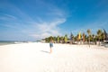 Cute stylish girl in blue dress standing on the amazing beach with wite sand, holding smartphone in her hands. She has Royalty Free Stock Photo