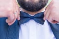 Cute stylish groom in a blue suit, blue necktie and white shirt. Close-up of a gentleman wearing blue Tie straightens his bowtie.