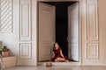 A cute stylish young girl in an elegant burgundy dress sits in the doorway to her room. Teenager. Graduation in school, college