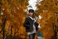 Cute stylish young woman fashion model in a trendy black hat with a leather bag posing in autumn park on a background of trees Royalty Free Stock Photo