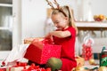 Cute super excited young girl opening large red christmas present while sitting on living room floor. Candid family christmas time Royalty Free Stock Photo