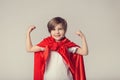 Cute superwoman kid in red cape shows her muscle