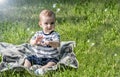 Cute Surprised baby boy whatching at the flying soap bubbles and sitting on green grass at summer sunny day