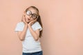 Cute surprised little caucasian girl in round glasses and hands near her face on a pink background with empty space Royalty Free Stock Photo