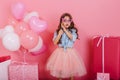 Cute surprised little girl with long brunette hair holding mask on face, looking to camera  on pink background Royalty Free Stock Photo