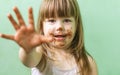 A cute, sweet little girl with chocolate smeared all over her face and fingers. A happy little girl with a dirty face is smiling.
