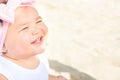 Cute Sweet 1 Year Old Baby Girl Toddler Sits on Beach Sand by Ocean Smiling. Sweet Face Expression. Bright Sunny Day. Parenting